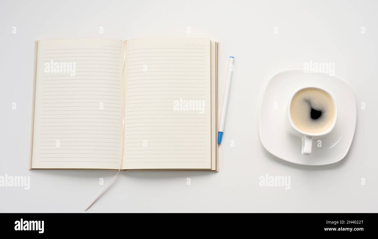 Open notebook with blank white sheets and a cup of coffee on a white table, workplace, top view Stock Photo