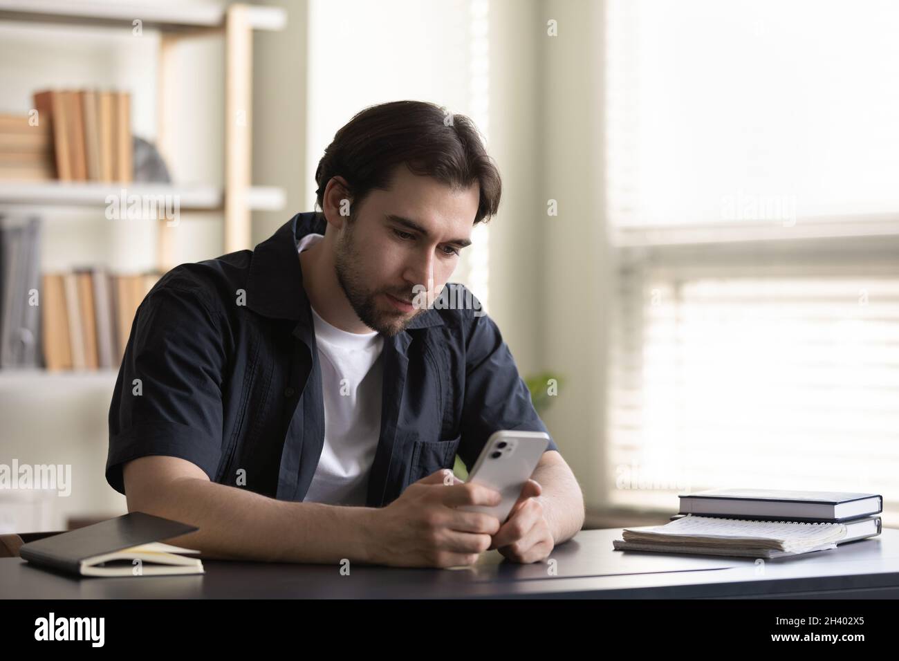 Happy young 30s man using cellphone sitting at table. Stock Photo