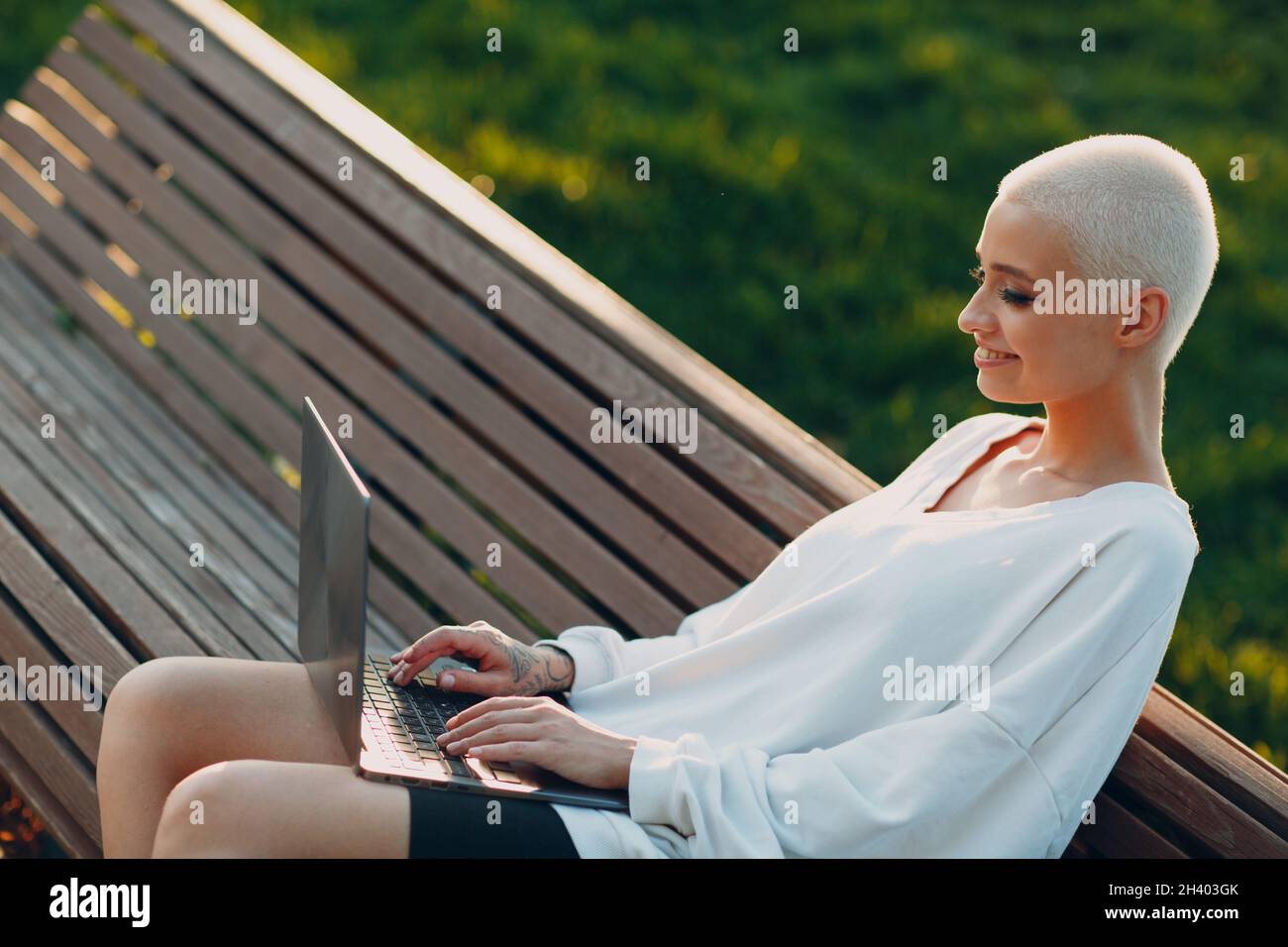 Millenial young woman blonde short hair outdoor smiling portrait with laptop. Stock Photo