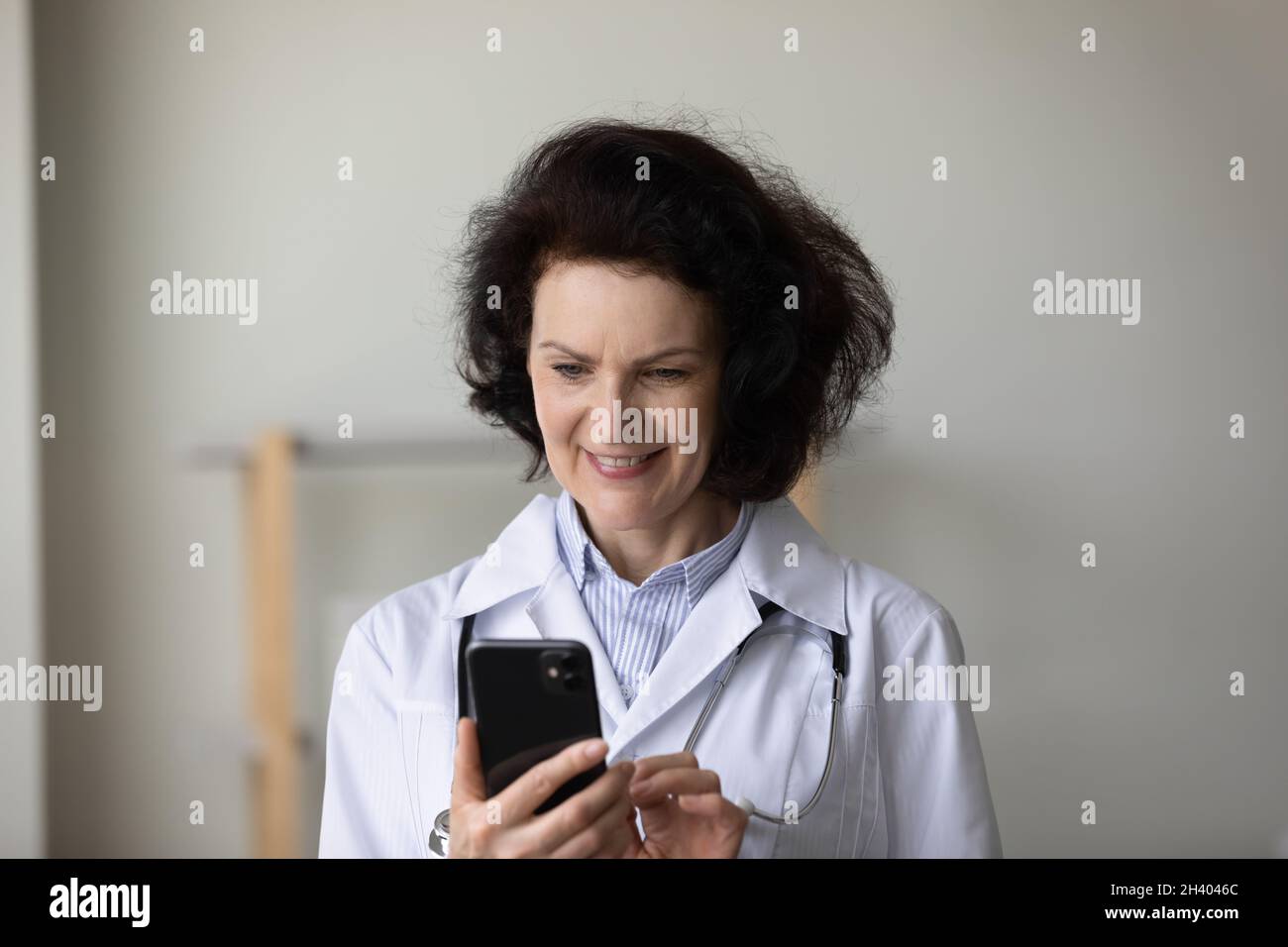 Happy middle aged female doctor using cellphone. Stock Photo
