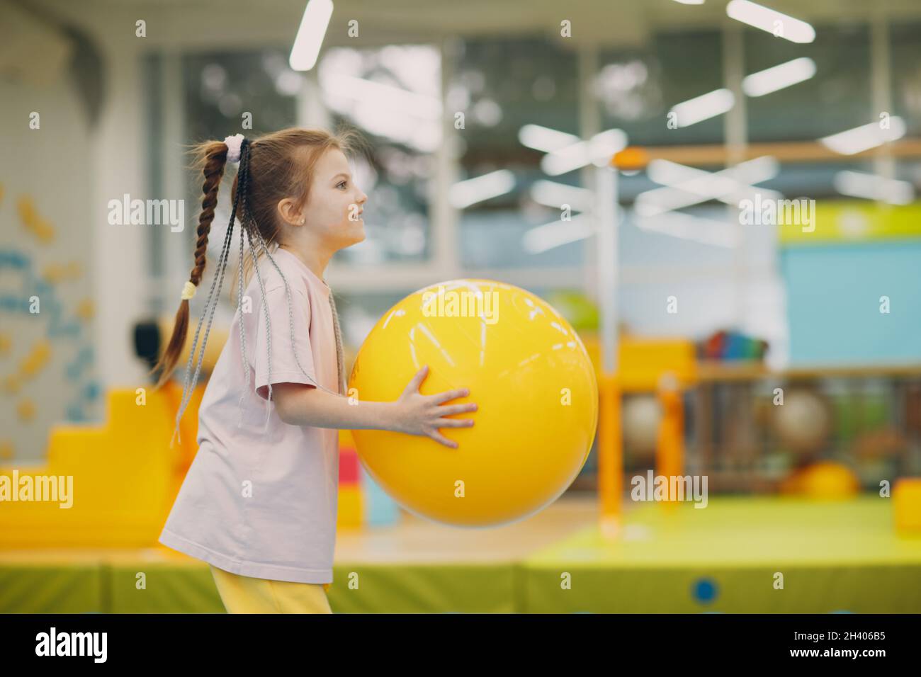 Little girl playing and doing exercises with big ball in gym at kindergarten or elementary