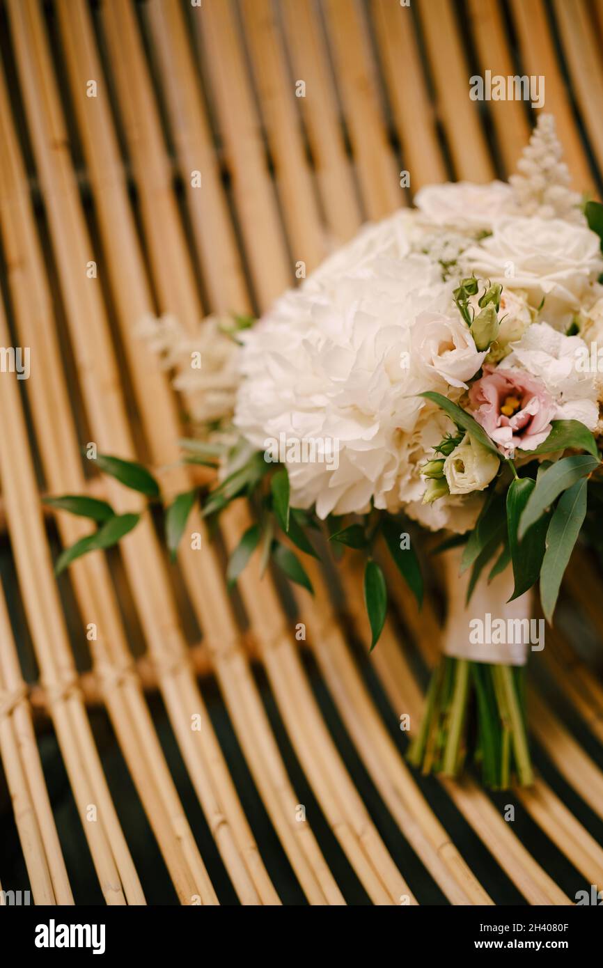 Bridal bouquet of white peonies, roses, pink eustoma, astilbe and branches of eucalypt tree on a straw chair Stock Photo