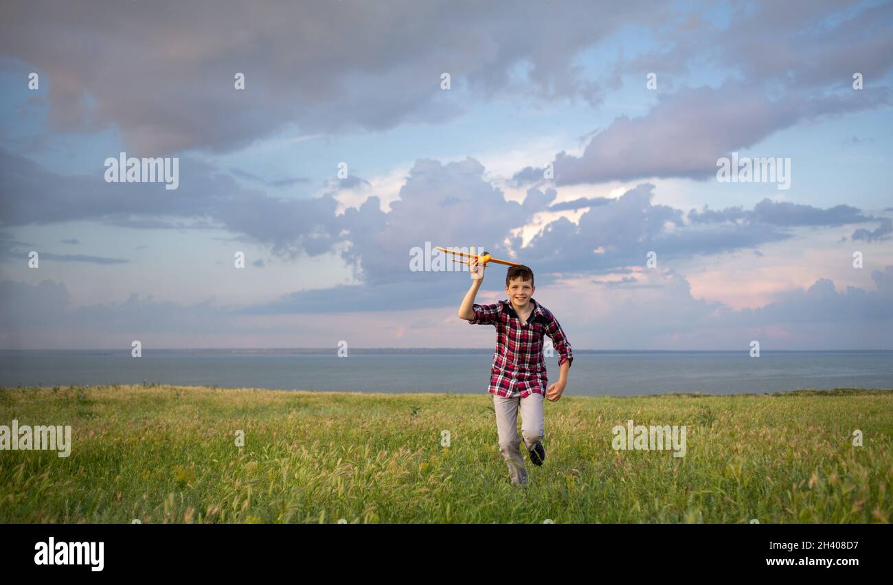Boy running across the field launches a toy plane into the sky at sunset cloudy background. A child walks alone and plays in nature. A teenage pilot Stock Photo