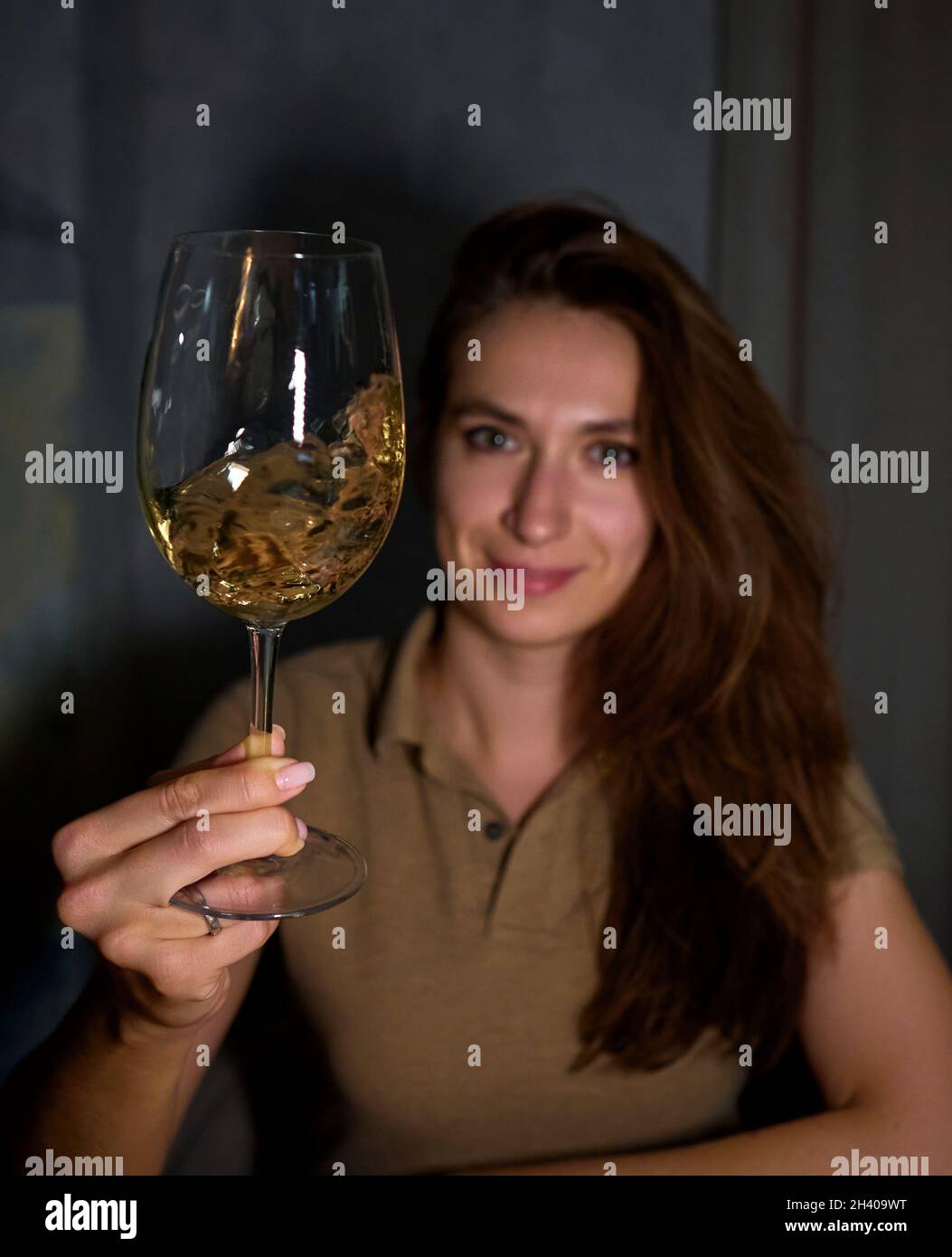 a girl in a white sweater holds a glass of sparkling wine on her outstretched hand Stock Photo