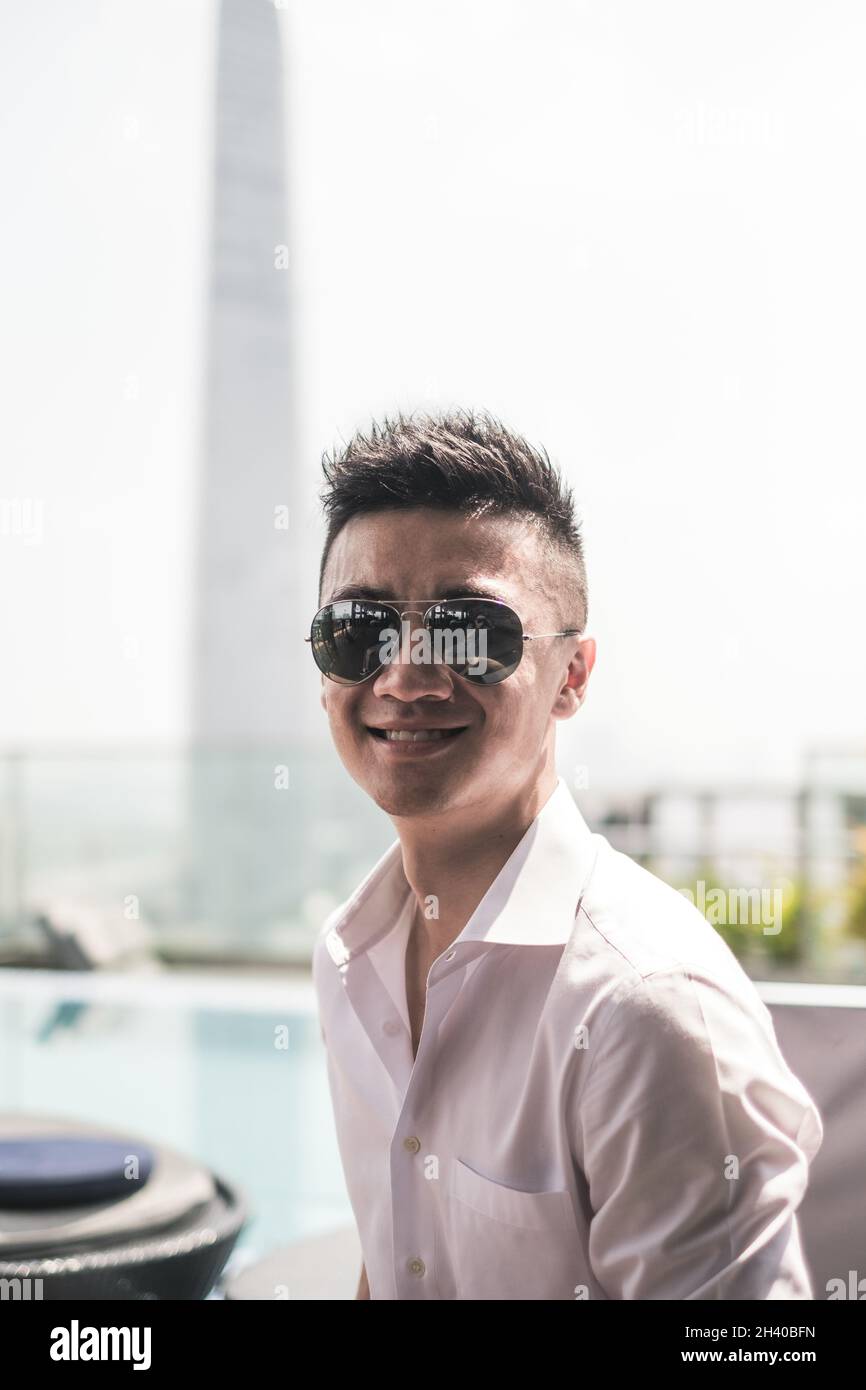 Portrait of handsome young Asian man sitting on the rooftop near the swimming pool. Chinese guy, millennials life, lifestyle in the city, Modern Asia Stock Photo