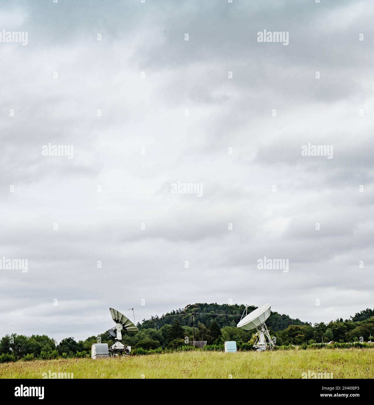 Large radio telescope is situated under green hills against cloudy sky Stock Photo