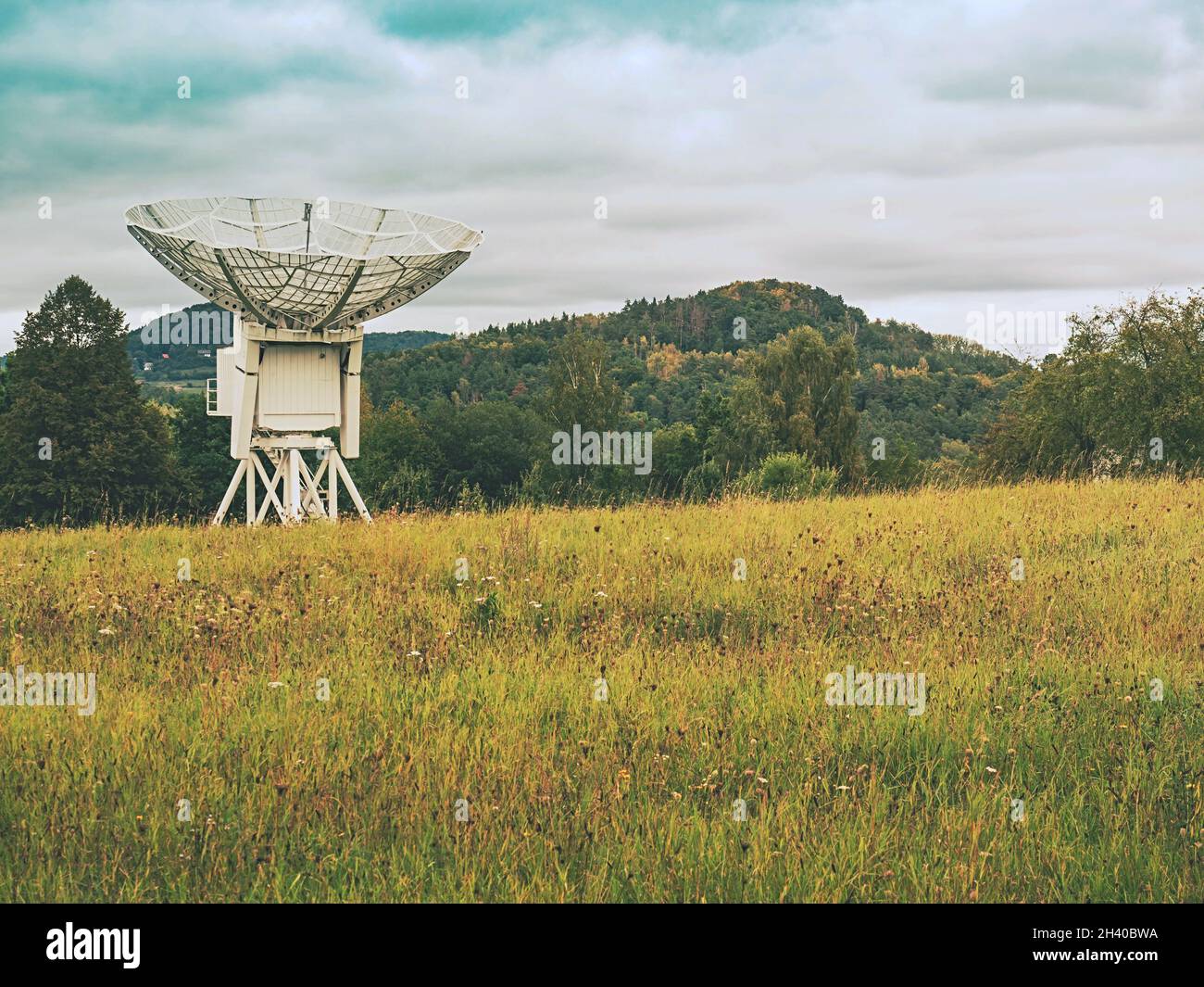 Large radio telescope is situated under green hills against cloudy sky Stock Photo
