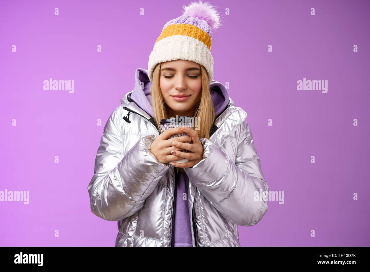 Charming tender romantic blond girl sniffing nice smell warm tasty coffee holding take-away cup warm hands close eyes look delig Stock Photo