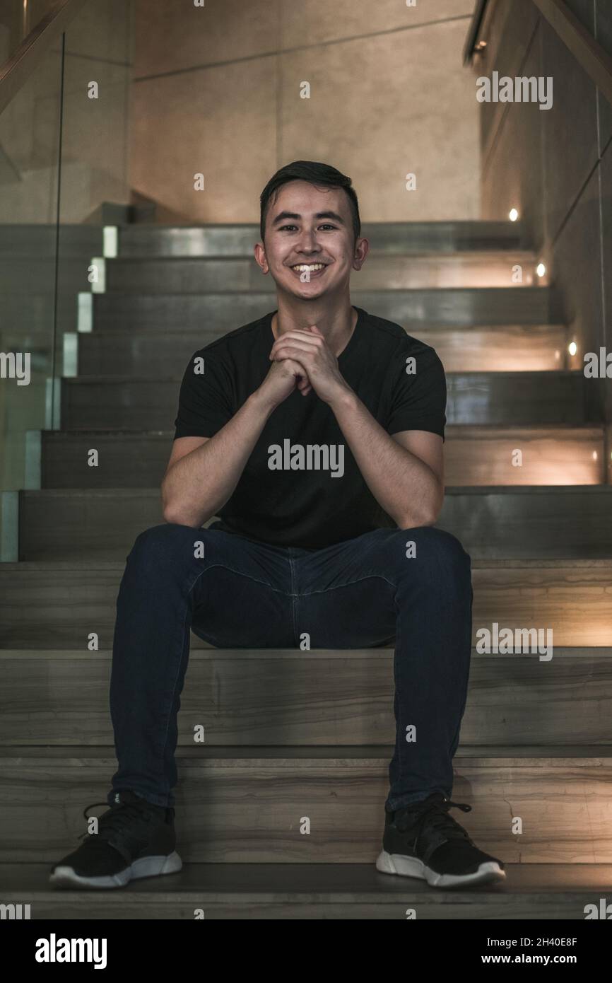 Asian young handsome man sitting on the stairs shop and smiling ...