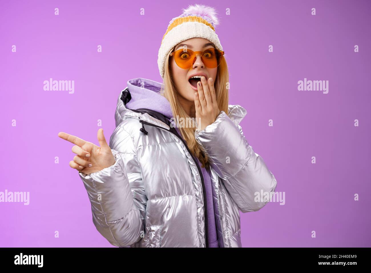 Amazed speechless surprised attractive stylish blond girlfriend in sunglasses, silver glittering jacket hat drop jaw impressed w Stock Photo