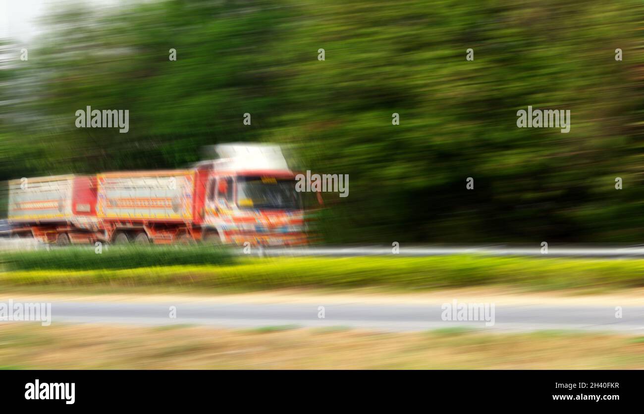Blurred, unrecognizable trucks carry goods along highway. Stock Photo