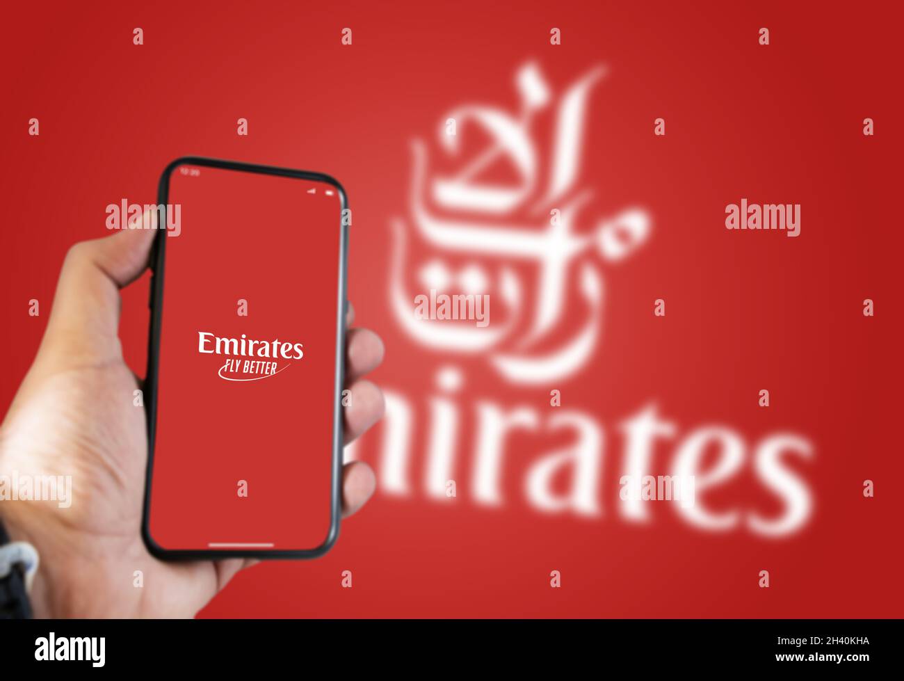 Dubai, UAE, July 2021: A hand holding a phone with the Emirates airline app on the screen and the Emirates logo Blurred on a green background. Stock Photo