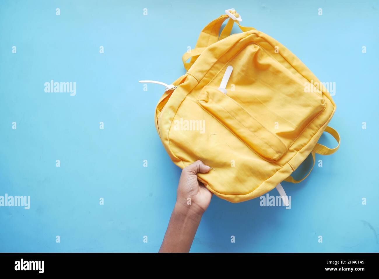 child boy hand holding a yellow backpack on blue  Stock Photo