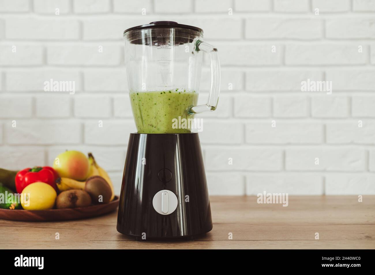 Stationary blender with healthy green smoothie and ingredients on table in kitchen Stock Photo