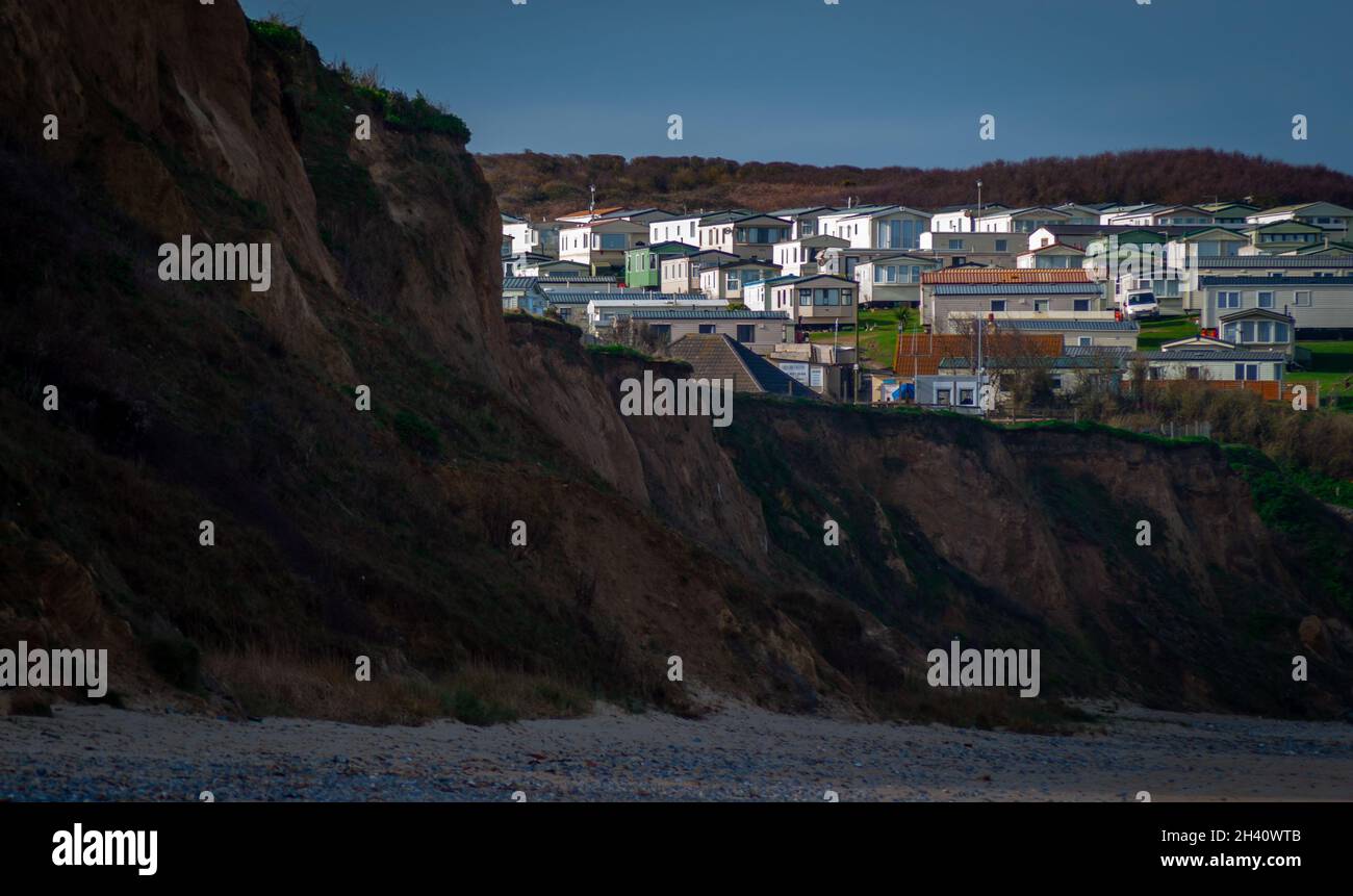 Touring and static caravans nestled in a dip at the top of sandstone cliffs above a shingle beach Stock Photo