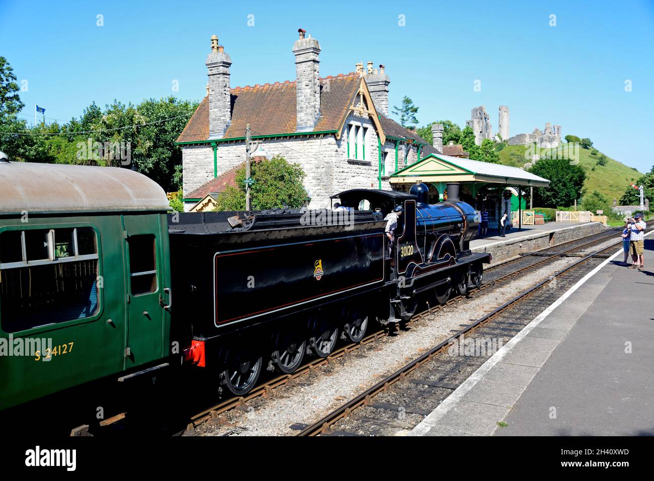 LSWR T9 Class 4-4-0 steam train entering the railway station with the castle to the rear, Corfe, Dorset, England, UK, Western Europe. Stock Photo