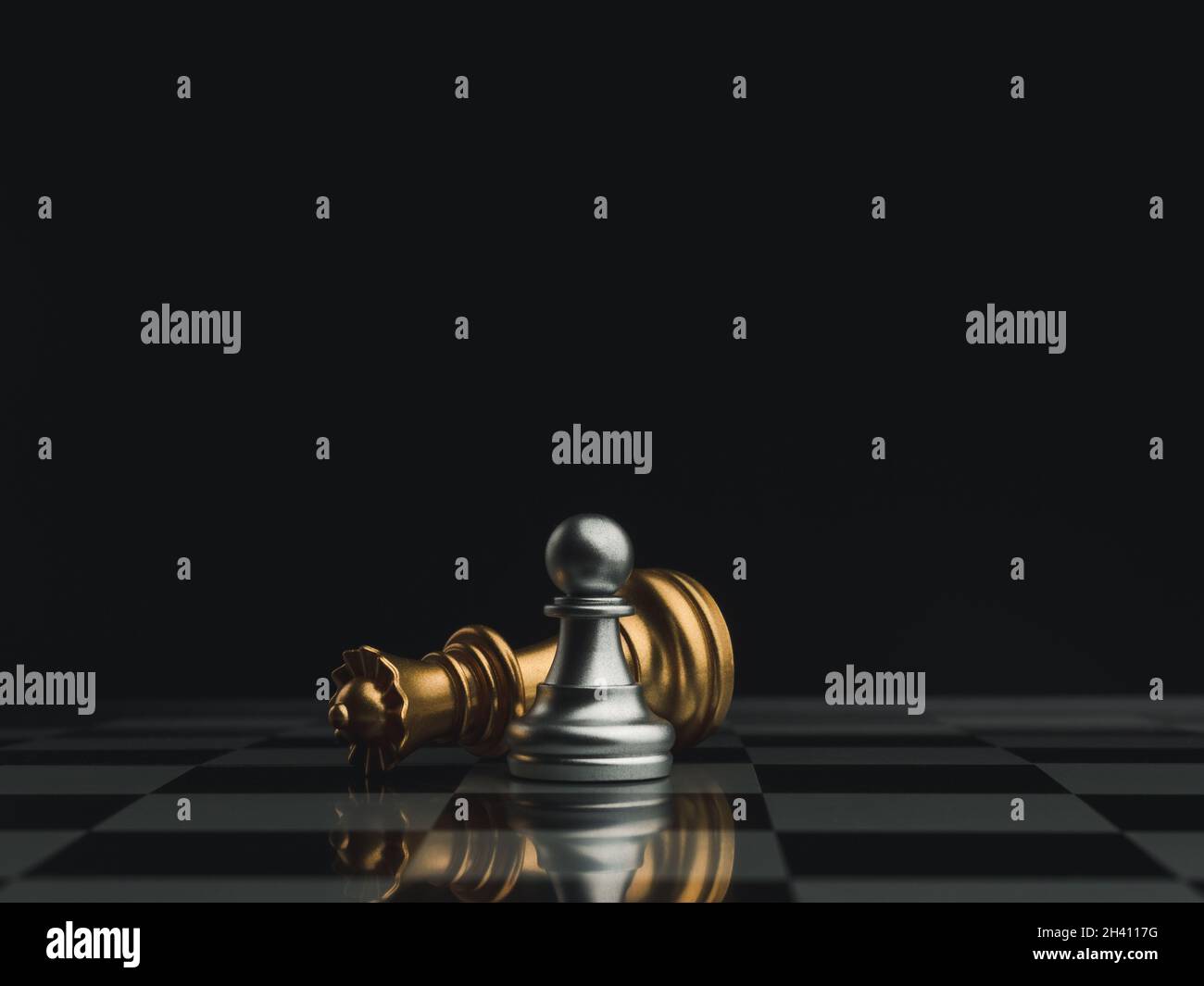 A little silver pawn chess piece standing with the win near a fallen golden queen chess piece on a chessboard on dark background. Leadership, winner, Stock Photo