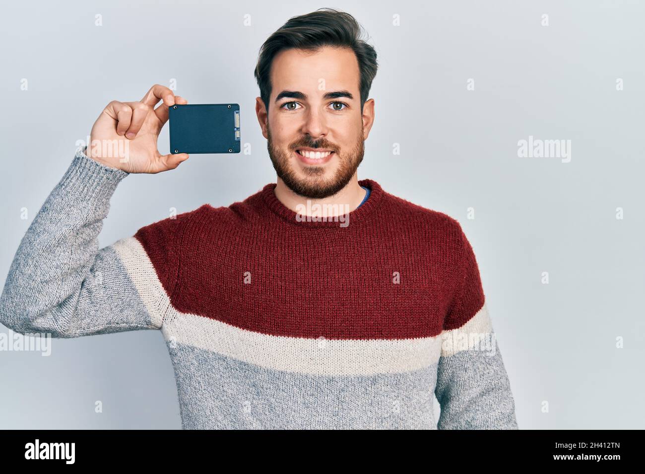 Handsome caucasian man with beard holding ssd memory looking positive ...