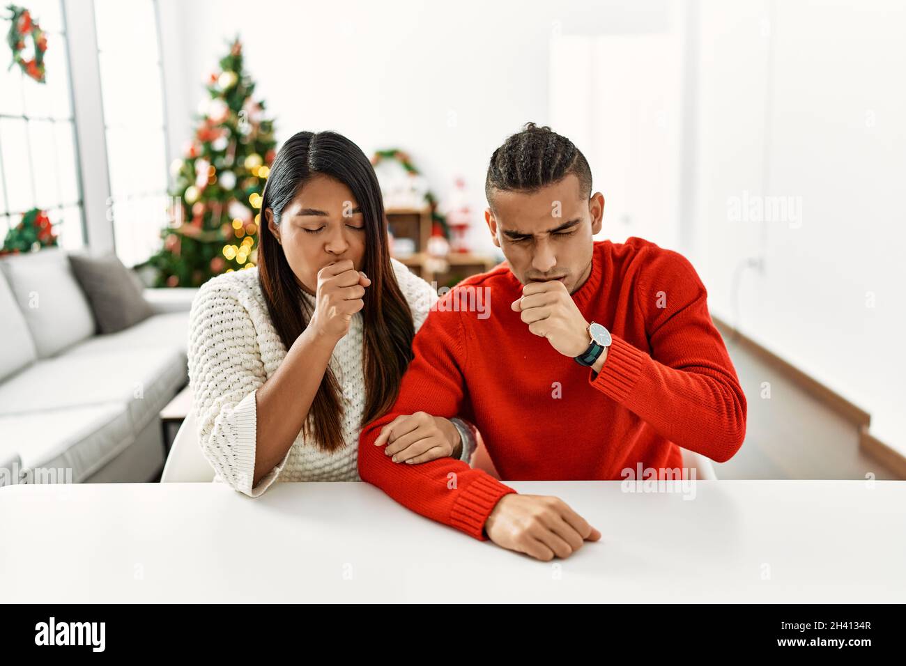 Young latin couple sitting on the table by christmas tree feeling
