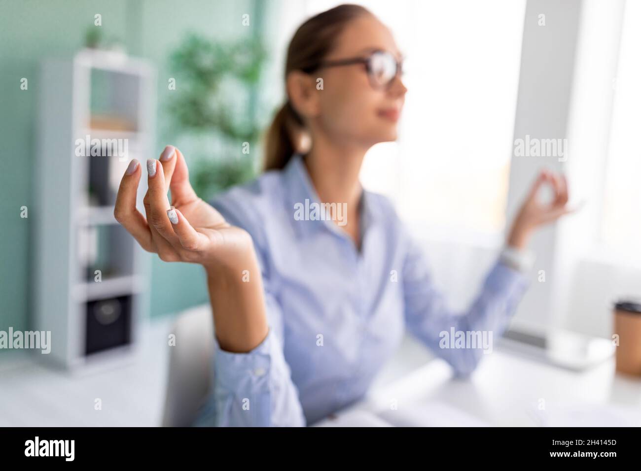 Office meditation. Calm female entrepreneur meditating and relaxing during stressful day at workplace, focus on hand Stock Photo