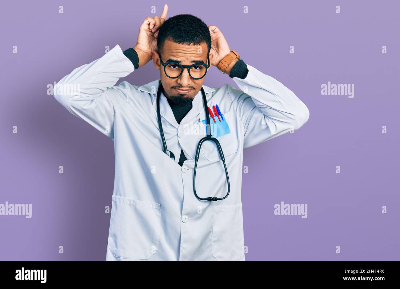 Young african american man wearing doctor uniform and stethoscope doing  bunny ears gesture with hands palms looking cynical and skeptical. easter  rabb Stock Photo - Alamy