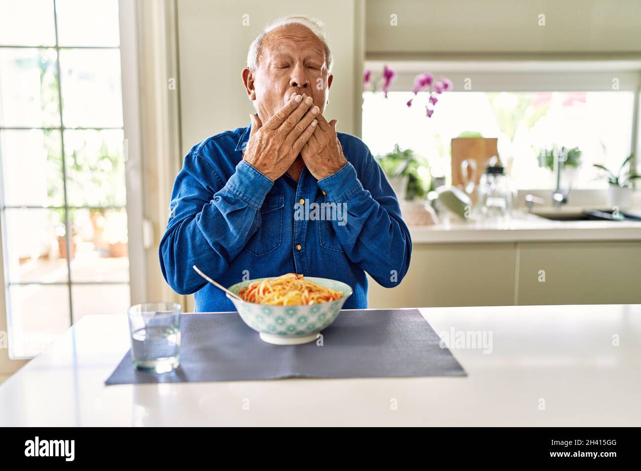 Senior man with grey hair eating pasta spaghetti at home bored yawning