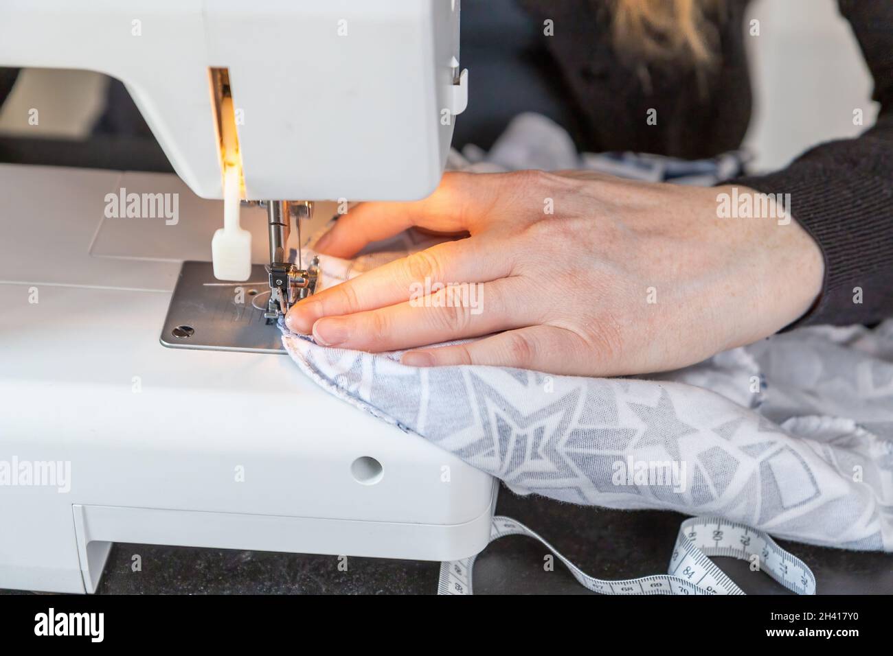 Female hands are sewing at home using a sewing machine closeup. Horizontally. Stock Photo