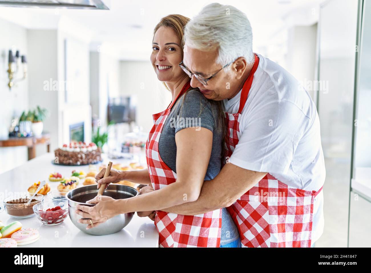 Middle age hispanic couple smiling happy and hugging cooking sweets at ...