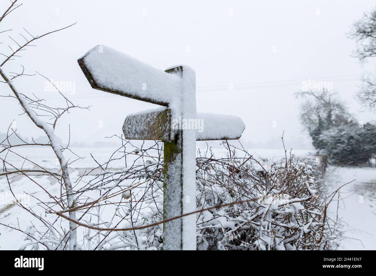 A countryside sign post that displays public footpaths totally covered in snow and unreadable Stock Photo