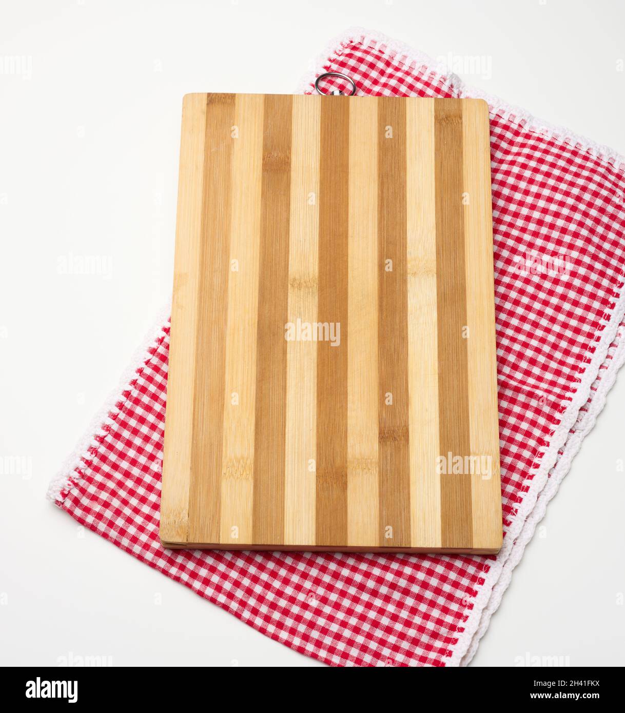 Empty rectangular wooden kitchen cutting board and red towel in a white cage on a white table, top view Stock Photo