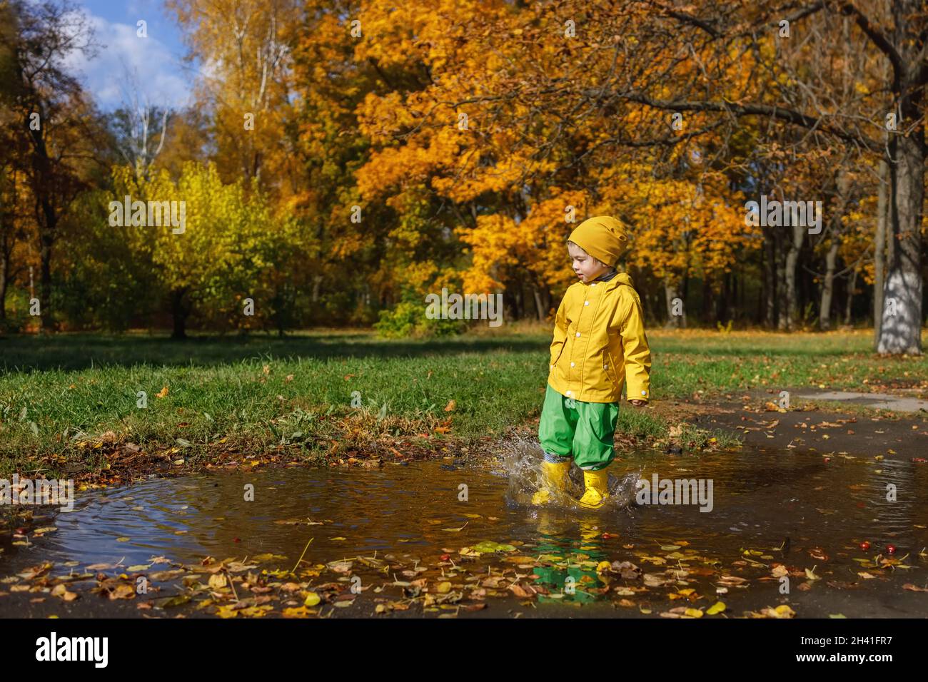 child boy in yellow raincoat have fun with puddle Stock Photo