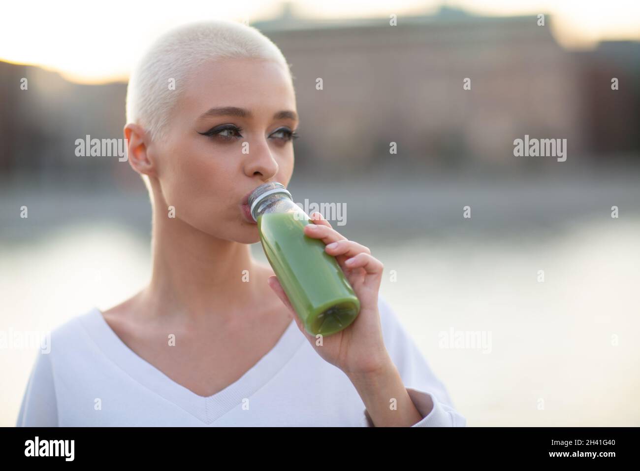 Millenial young woman blonde short hair outdoor with green smoothie Stock Photo