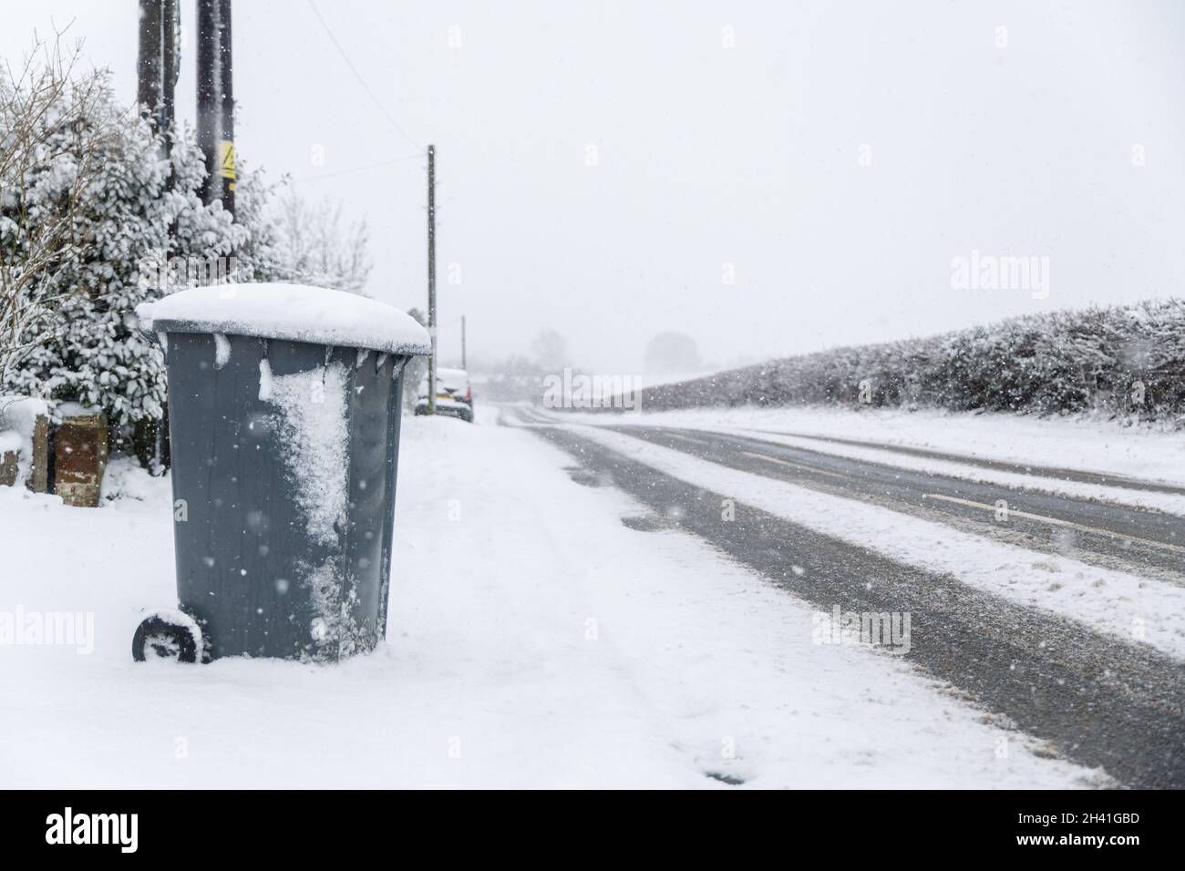 A council wheelie bin sitting by the side of the road in a snow covered