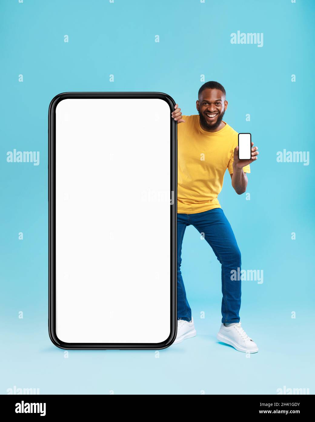 Handsome black guy standing near giant cellphone with blank screen, showing mobile  device on blue background, mockup Stock Photo - Alamy