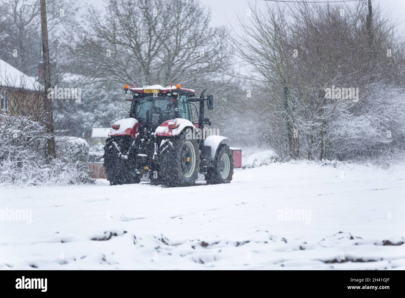 Woodbridge Suffolk UK February 07 2021: A red tractor parked up on the edge of a farm field in a heavy blizzard in the British countryside Stock Photo