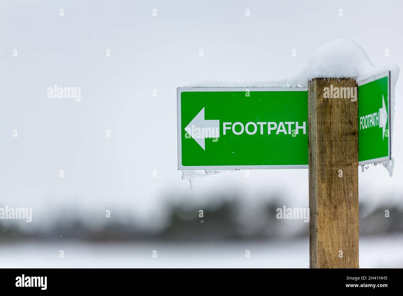Public footpath sign pointing to the left with snow and icicles on it in rural British Countryside Stock Photo