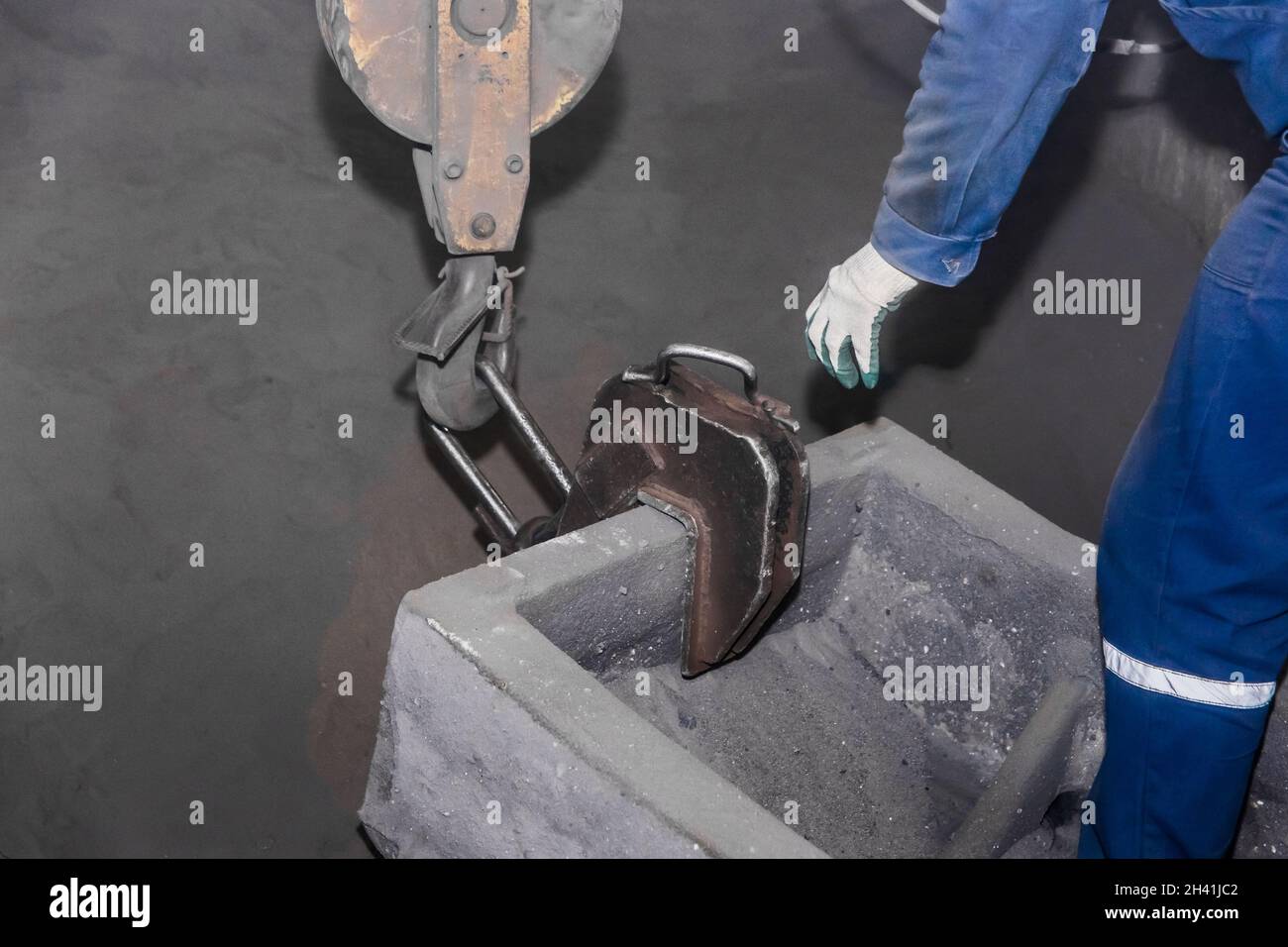 A man in overalls attaches an iron hook of a lifting mechanism to cast-iron tubing, reinforced concrete structures made of cast products at an industr Stock Photo