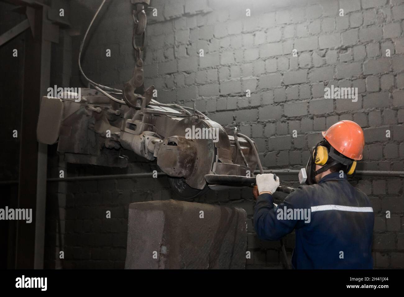 A working man in a protective helmet, respirator and overalls controls