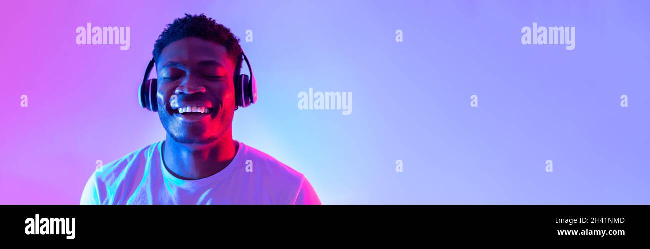 Handsome young black man wearing headphones, listening to music with closed eyes in neon light, banner design Stock Photo