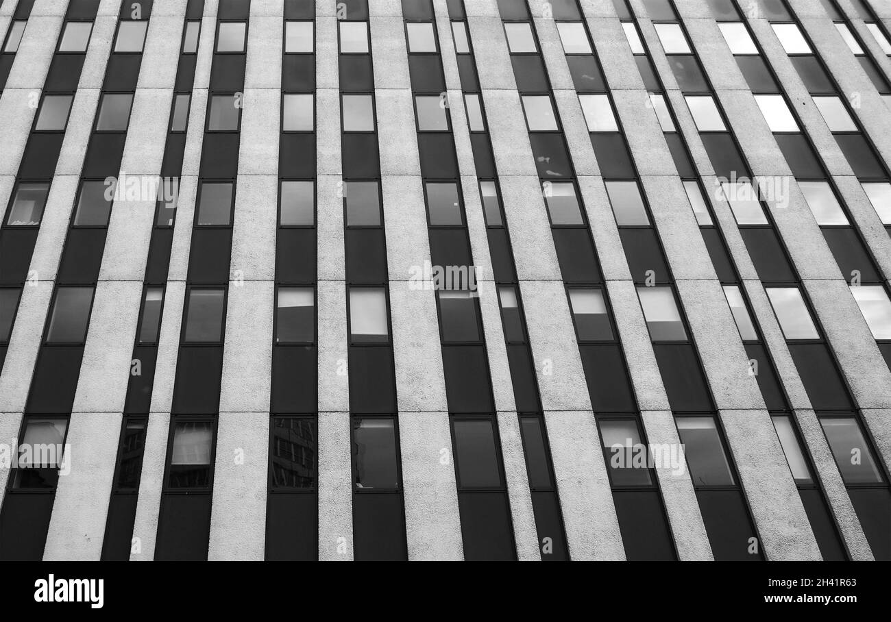 Close up perspective detail of tall high rise brutalist style office building with white vertical concrete lines and dark window Stock Photo