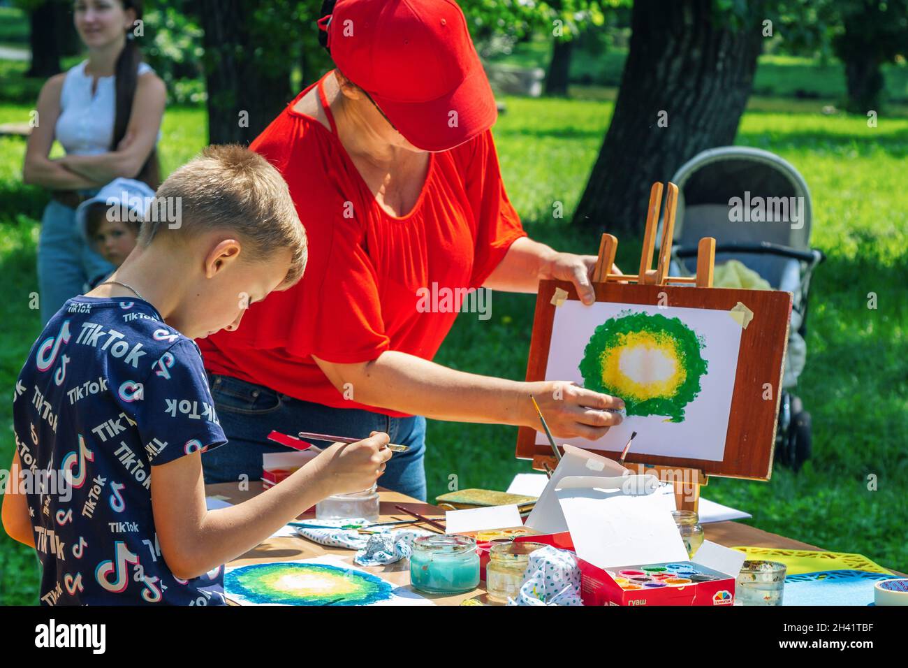 Zaporizhia, Ukraine- June 19, 2021: Charity Family festival:  woman – volunteer explaining to a boy how to paint the picture with watercolor paints at Stock Photo