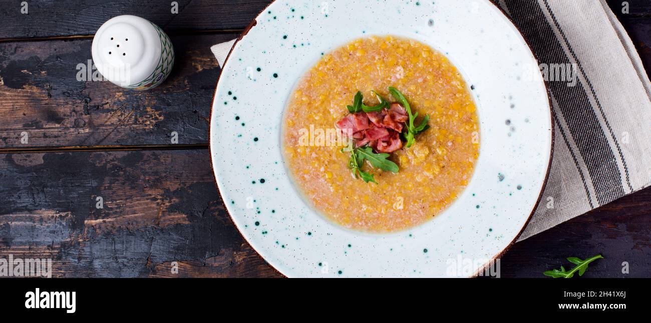 Homemade red lentil cream soup with bacon and arugula in a white plate on an old wooden background. Rustic style. Top view. Stock Photo