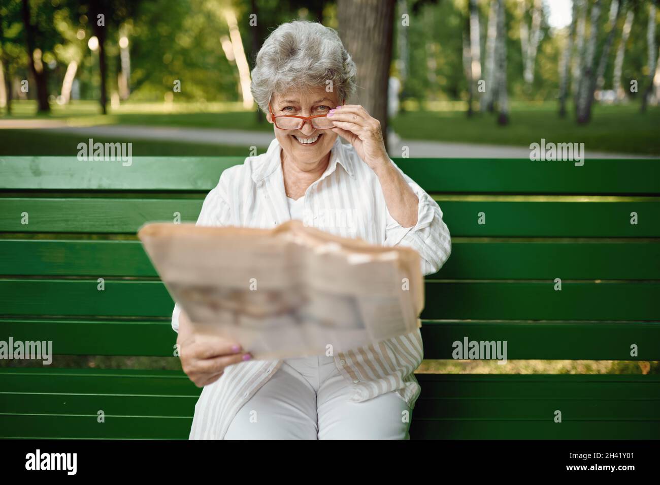 An elderly woman in glasses reading newspaper Stock Photo