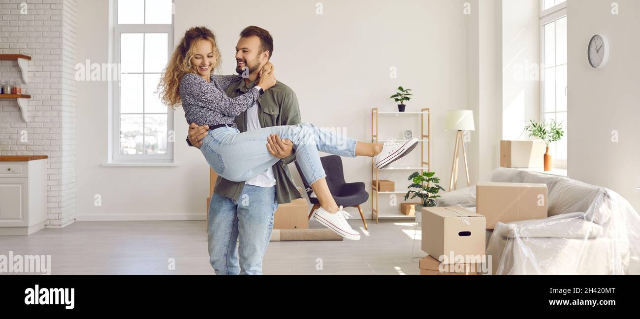 Happy loving husband holding his beloved wife in his arms in their new house during move. Stock Photo