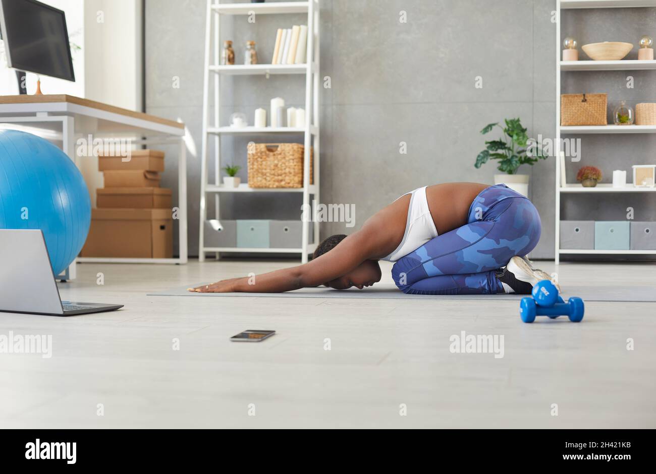 African american woman doing sports exercises at home in front of laptop during online broadcast. Stock Photo
