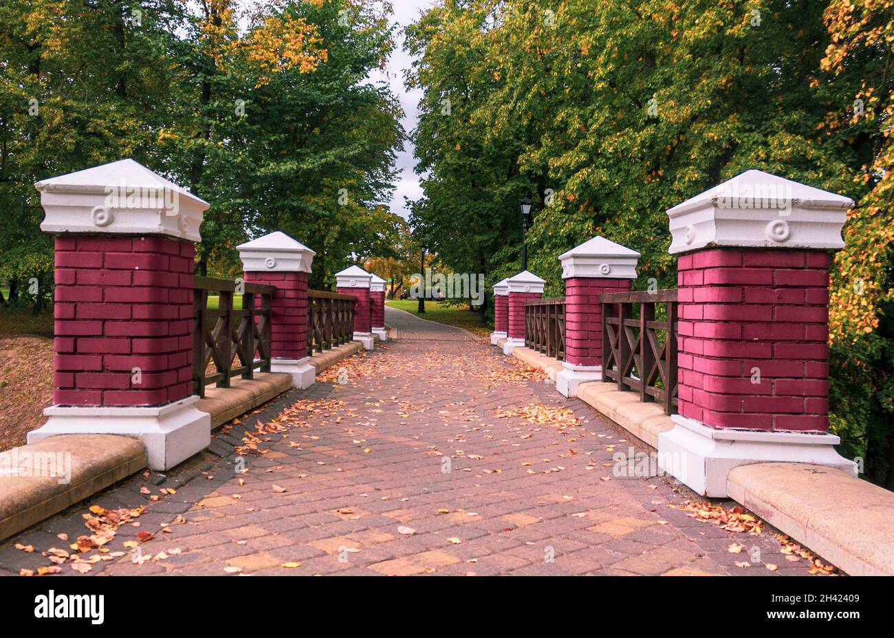 Red brick columns on the fence of a bridge in an autumn park with yellowed trees. Beautiful autumn landscape in the park. Stock Photo