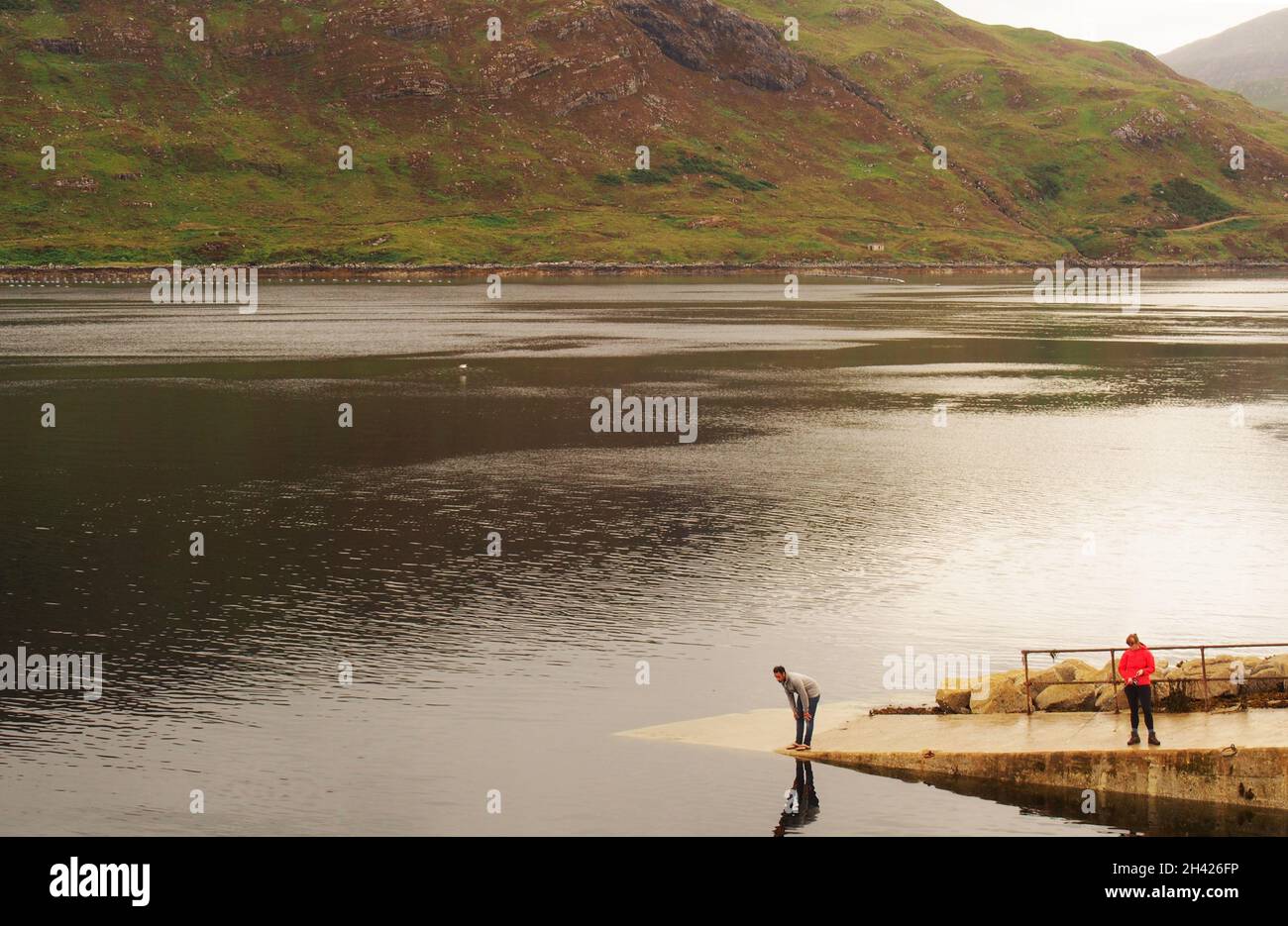 A young man and woman fishing on a slipway at Kylesku pier by Loch Gleann |Dubh, Sutherland, Scotland Stock Photo