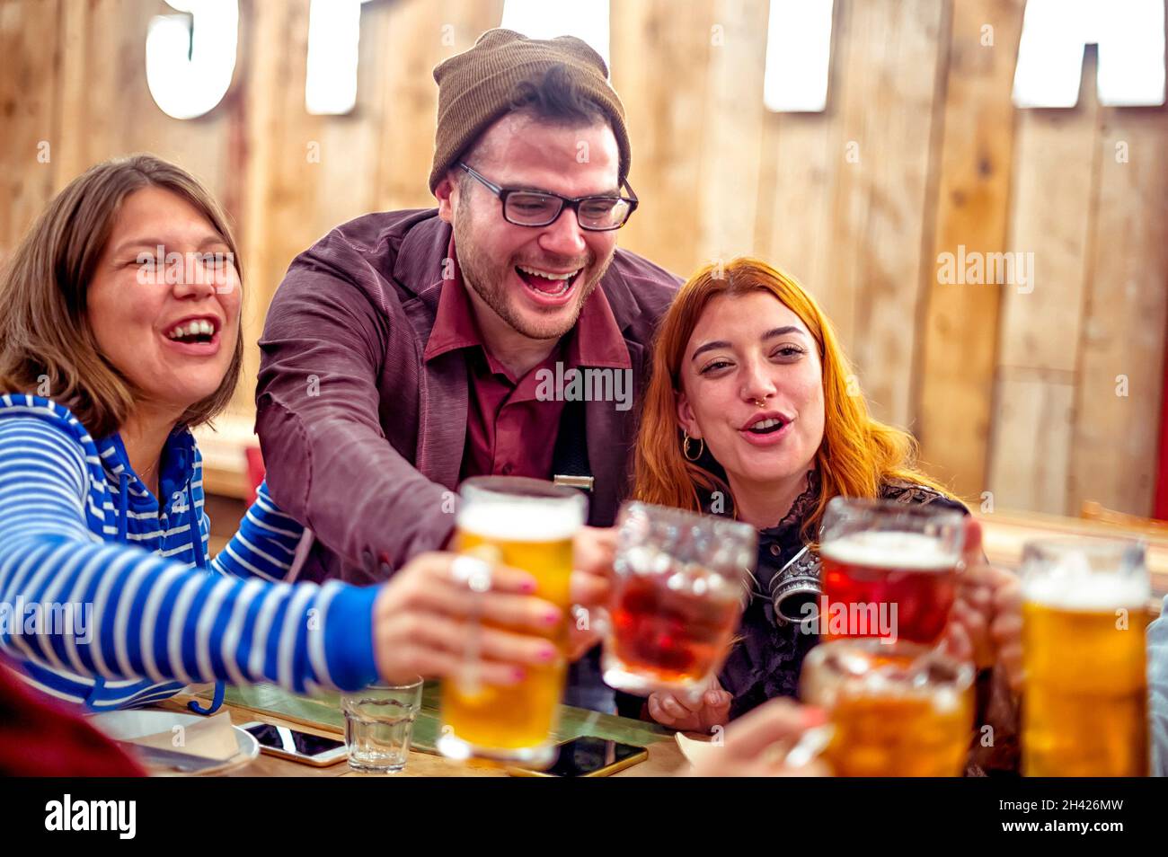 Group of happy friends clinking draft beer mugs in pub - Smiling boy and girls with beer in their hands toasting at the restaurant in the happy hour t Stock Photo