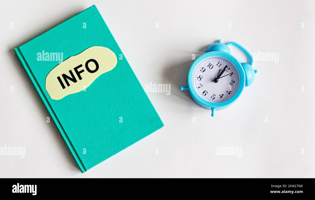 On a green notebook is a piece of paper with the word INFO on a white background next to the alarm clock. Business concept. Search idea Stock Photo
