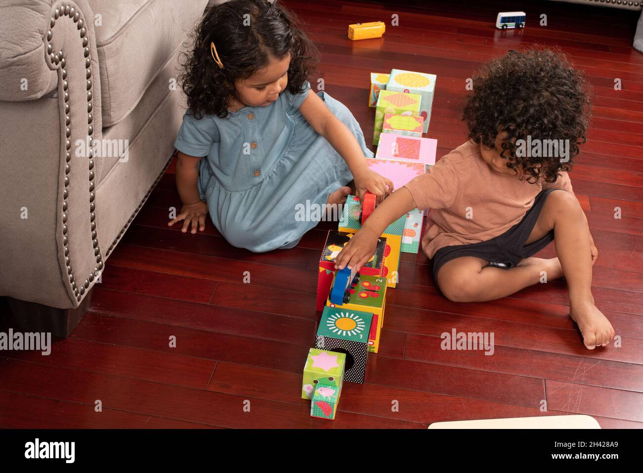 Two year old fraternal twins, boy and girl,  playing with toy cars driving them on road made of cardboard blocks Stock Photo